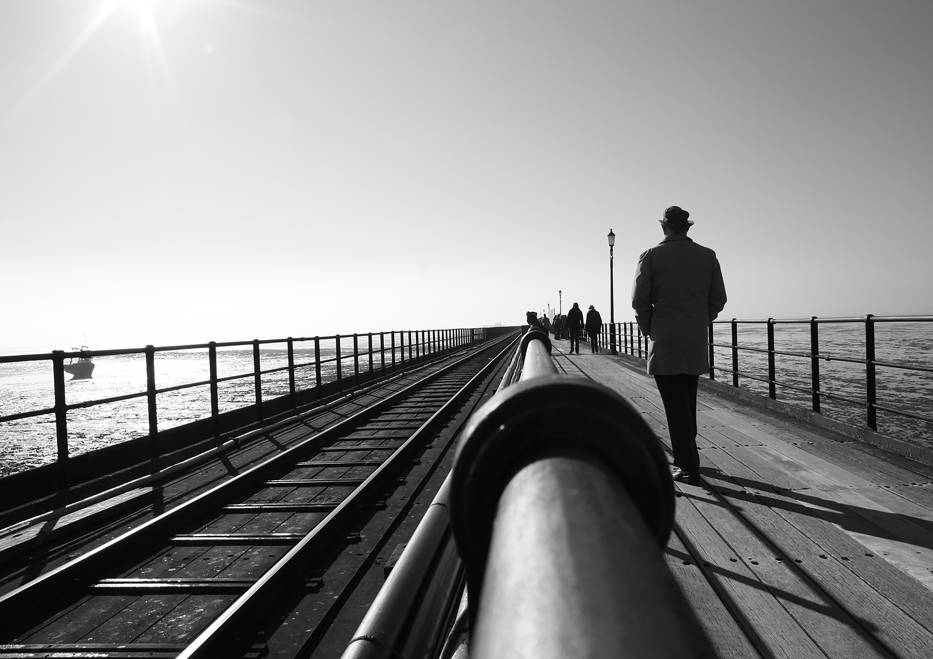 Black-and-white view along Southend Pier, with visitors walking beside the pier railway tracks.